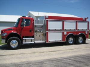 Osco Tank and Truck Sales Dominator fire truck with a Freightliner red cab and four roll-up stainless steel equipment access panels on the side of the truck.