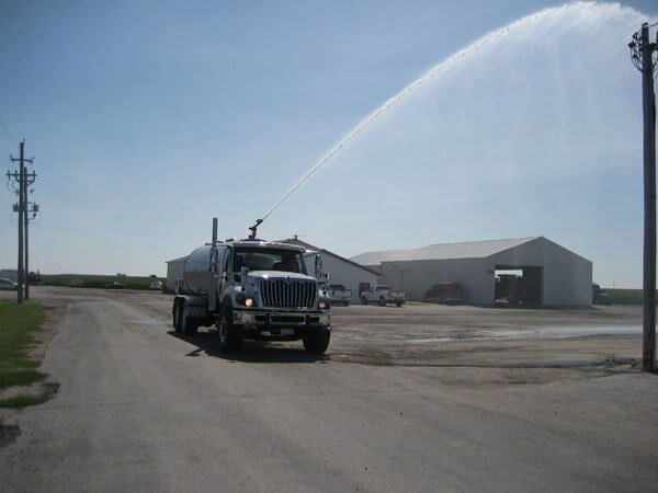 Osco Tank and Truck Sales water truck shooting an arch of water from a water cannon mounted on top of the tanker truck.