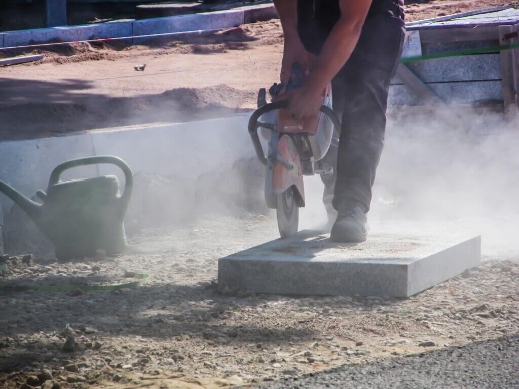 Dust rise while a worker saws into concrete at a construction site
